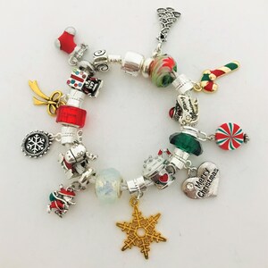 May include: A festive Christmas charm bracelet with silver beads and a variety of holiday-themed charms. Charms include a snowflake, candy cane, Santa, gift box, and a heart that says "Merry Christmas". The bracelet is on a white background.