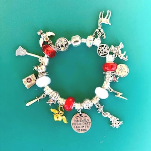 May include: Silver charm bracelet with various charms, including a broom, a letter, a golden winged key, and a charm that says "I solemnly swear that I am up to no good." The bracelet also features red and white beads.