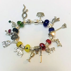 May include: A charm bracelet with various silver charms and colorful beads. Charms include a snake, a crown, a broom, a bear, a sword, and a goblet. The beads are in shades of green, blue, yellow, red, and gray.