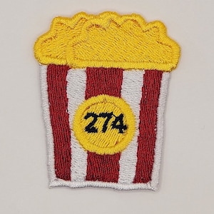 May include: Red and white striped popcorn bucket with a yellow circle containing the number 274. The top of the bucket is yellow and resembles popcorn.