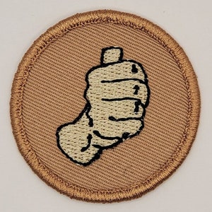 May include: A brown embroidered patch with a white hand giving a thumbs up.