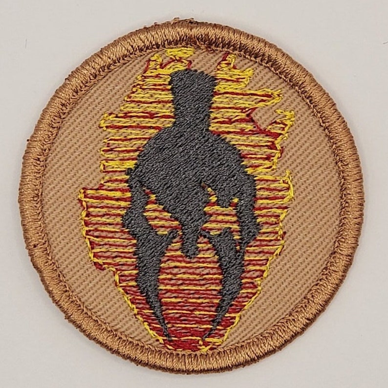 May include: A round, tan embroidered patch with a black silhouette of a Spartan helmet in a red and yellow flame design.