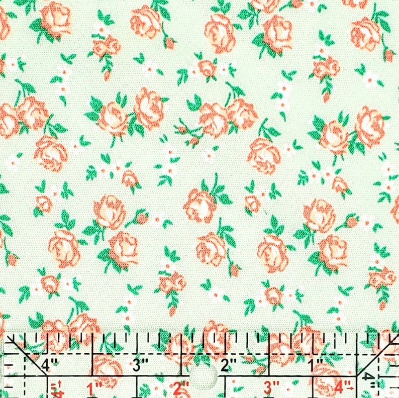 May include: A green fabric with a repeating pattern of small pink roses. The fabric is measured with a ruler in inches.