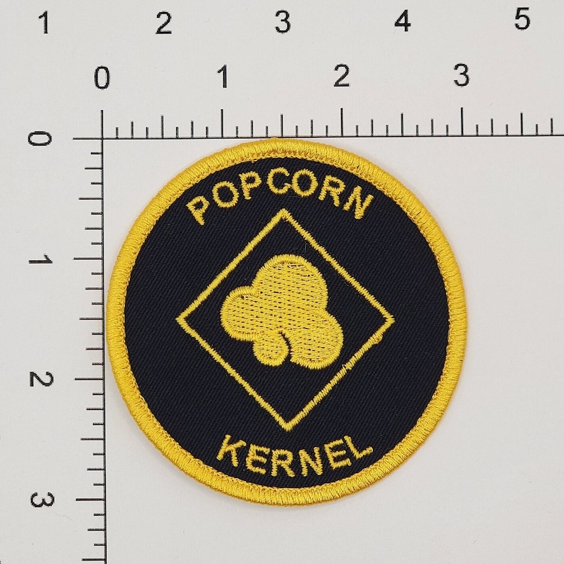 May include: A black and yellow embroidered patch with the words "POPCORN KERNEL" and a yellow popcorn kernel inside a yellow diamond.