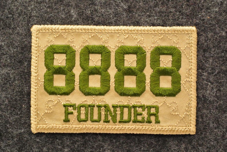 May include: Embroidered patch with the word "FOUNDER" below four green 8s. The patch is rectangular with a beige background and a decorative border. The background is a textured, patterned fabric.