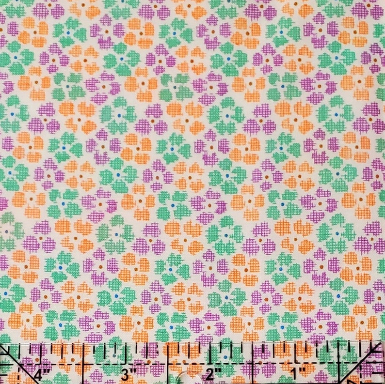 May include: A fabric with a repeating floral pattern in orange, purple, and green on a cream background. The image includes a ruler at the bottom, showing measurements in inches, which are equivalent to centimetres.