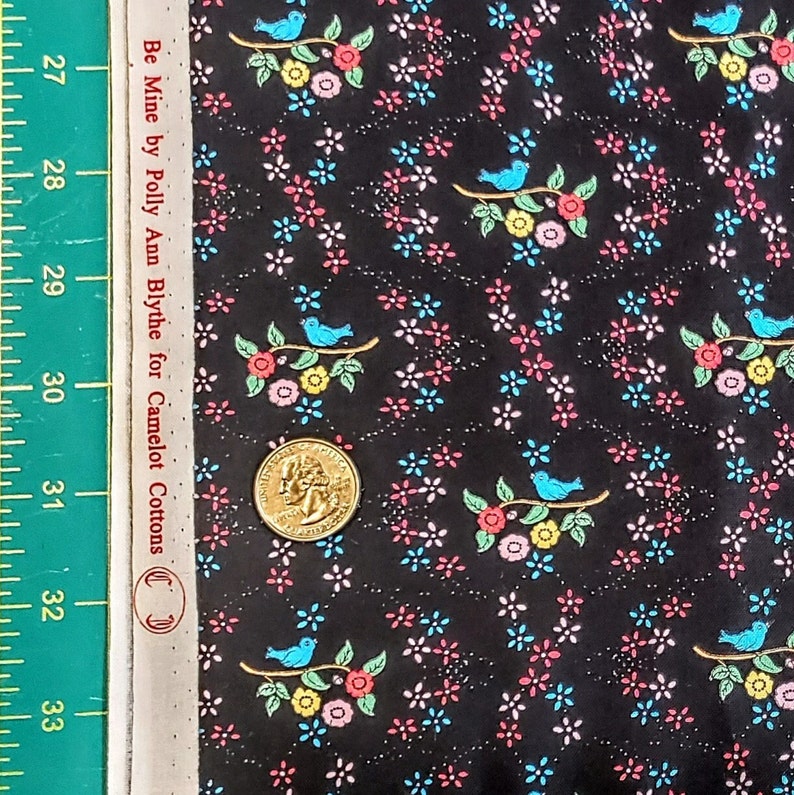 May include: Black fabric with a repeating pattern of blue birds perched on branches with pink, yellow, and green flowers. The fabric has a small, white, sparkly pattern throughout. The text "Be Mine by Polly Ann Blythe for Camelot Cottons" is printed on the side of the fabric.