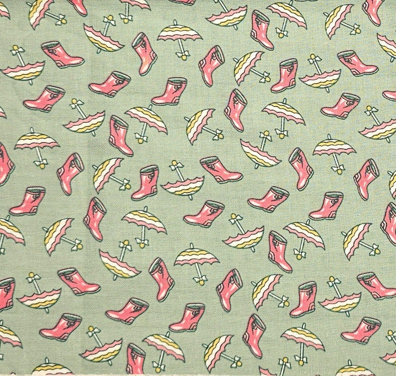 May include: A green fabric with a repeating pattern of pink rain boots and yellow and white striped umbrellas.