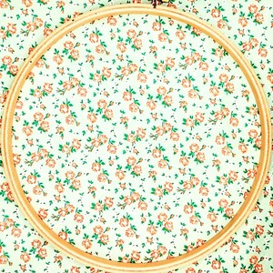 May include: A wooden embroidery hoop with a white fabric background featuring a repeating pattern of small orange flowers.