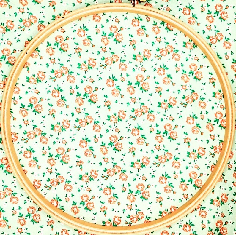 May include: A wooden embroidery hoop with a white fabric background featuring a repeating pattern of small orange flowers.