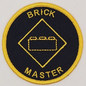 May include: A black and gold embroidered patch with the words "Brick Master" and a stylized image of a Lego brick.