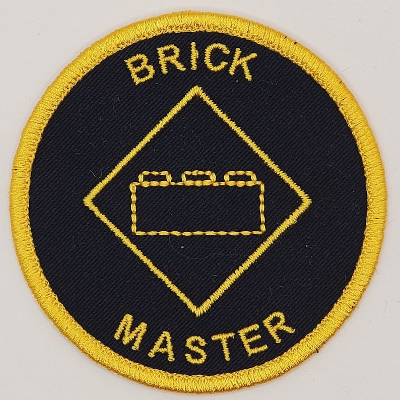 May include: A black and gold embroidered patch with the words "Brick Master" and a stylized image of a Lego brick.
