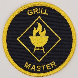May include: A yellow and black embroidered patch with the text "Grill Master" and a yellow diamond shape with a grill and flames inside.