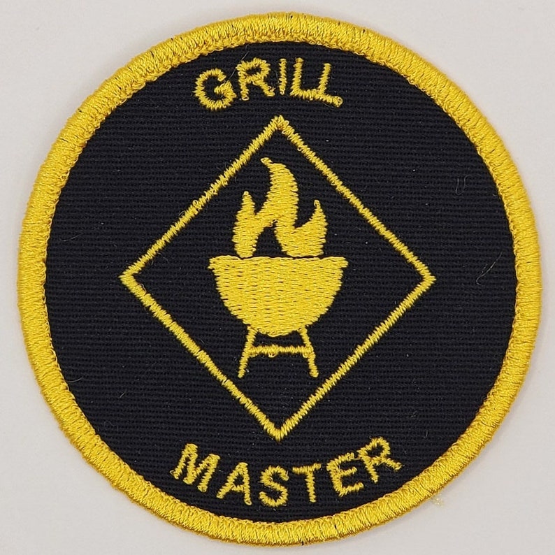 Peut inclure: Un &eacute;cusson brod&eacute; jaune et noir avec le texte "Grill Master" et un losange jaune avec un grill et des flammes &agrave; l'int&eacute;rieur.