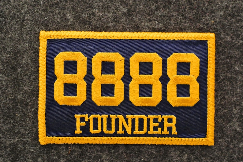 May include: A rectangular patch with a navy blue background and gold embroidered text and border. The number "8888" is prominently displayed above the word "FOUNDER". The patch is likely for a club or organization.