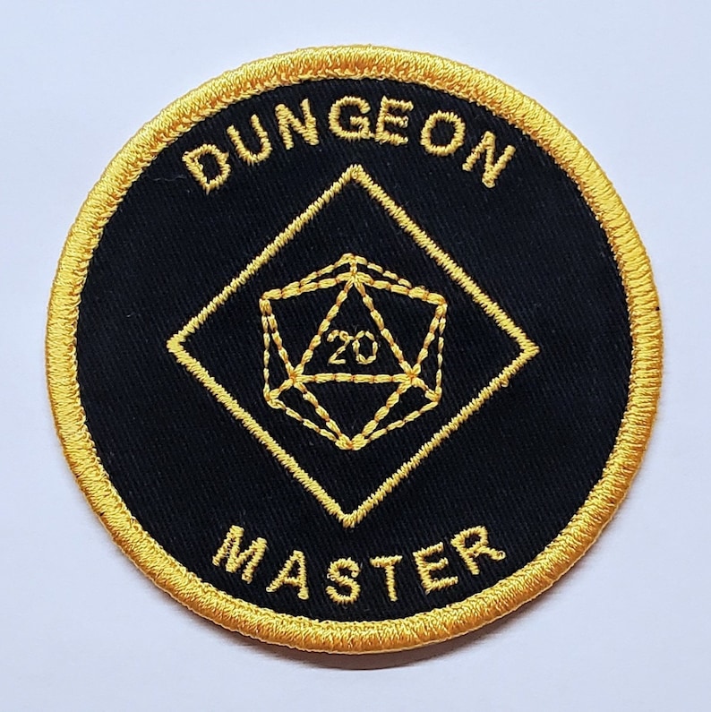 May include: A black and gold embroidered patch with the words "Dungeon Master" and a 20-sided die in the center.