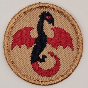 May include: A round, tan embroidered patch with a black dragon with red wings and tail. The dragon is facing right and has a red eye.