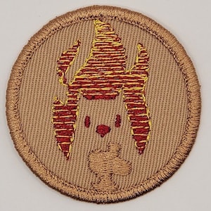 May include: Embroidered patch with a circular shape. The patch features a tan background with a detailed design of a stylized face and flame-like elements in red and yellow. The border is a stitched gold color.
