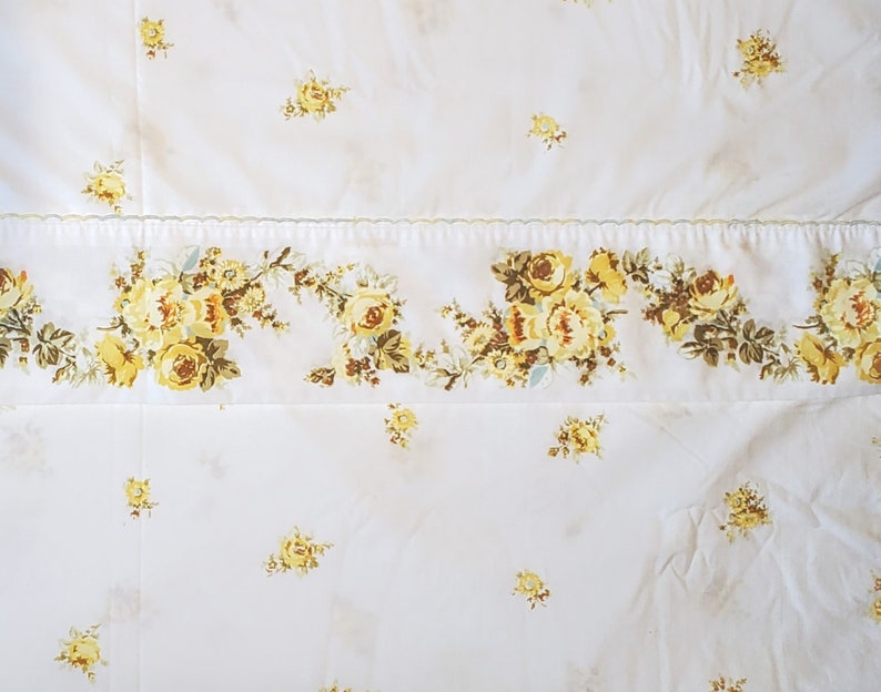 May include: White bedding with a yellow floral pattern. The floral pattern is a border along the bottom of the bedding.
