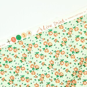 May include: A close-up of a light green fabric with a repeating pattern of small orange roses and white dots. The fabric has a label that reads "Line Dried by Mama's Cottons for".