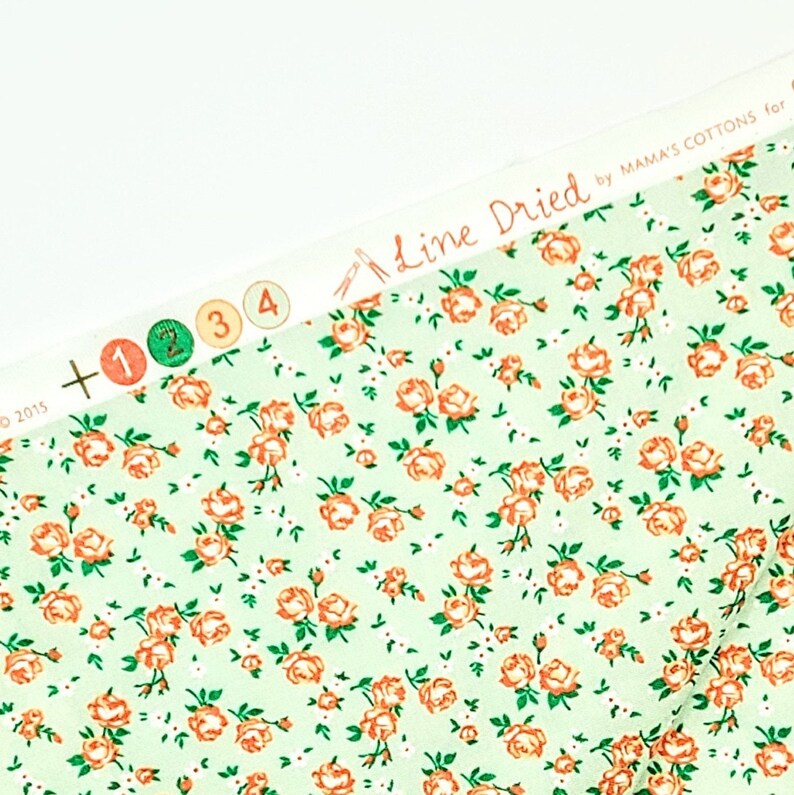 May include: A close-up of a light green fabric with a repeating pattern of small orange roses and white dots. The fabric has a label that reads "Line Dried by Mama's Cottons for".