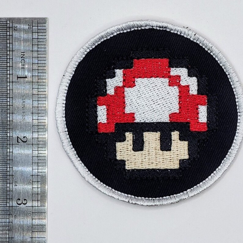 以下が含まれることがあります： 赤と白のスーパーマリオのキノコが刺繍された黒と白のパッチ
