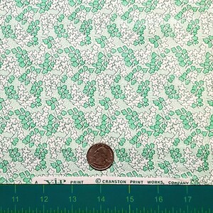 Pu&ograve; includere: Un primo piano di un tessuto verde e bianco con un motivo ripetitivo di piccoli fiori bianchi e foglie verdi. Il tessuto &egrave; testurizzato e ha un aspetto vintage. Una moneta da 25 centesimi di dollaro americano &egrave; inclusa per la scala.