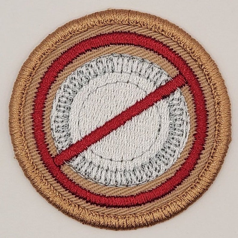 May include: A brown embroidered patch with a red circle and a diagonal red line through it. The circle has a white center with a gray ring around it.