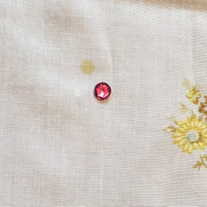 May include: A close-up of a white fabric with a red, hexagonal-shaped button.