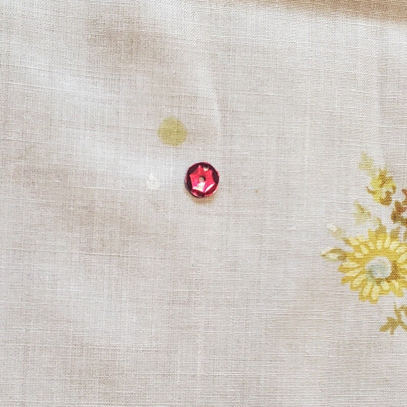 May include: A close-up of a white fabric with a red, hexagonal-shaped button.