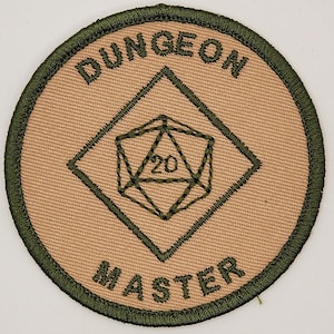 May include: A tan fabric patch with green embroidered text that reads "DUNGEON MASTER" and a green embroidered 20-sided die in the center.