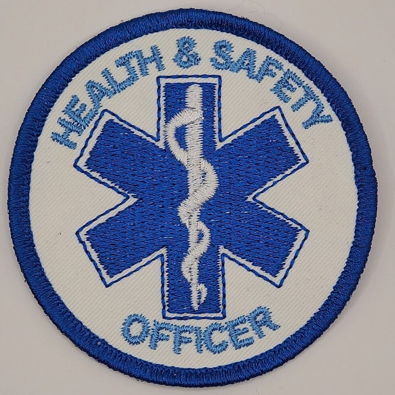 May include: A white embroidered patch with a blue star of life and the text "HEALTH & SAFETY OFFICER" in blue.