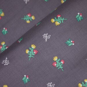 Op de afbeelding: Close-up van een gevouwen grijze stof met een herhalend bloemenpatroon. Het patroon bevat kleine boeketten van rode en gele bloemen met groene bladeren en witte gestileerde insectenontwerpen.