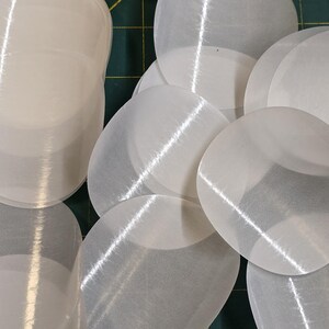 May include: A collection of translucent, oval-shaped, white objects. The objects are arranged on a green cutting mat with yellow grid lines. The objects have a slightly textured surface and appear to be made of a thin, flexible material.