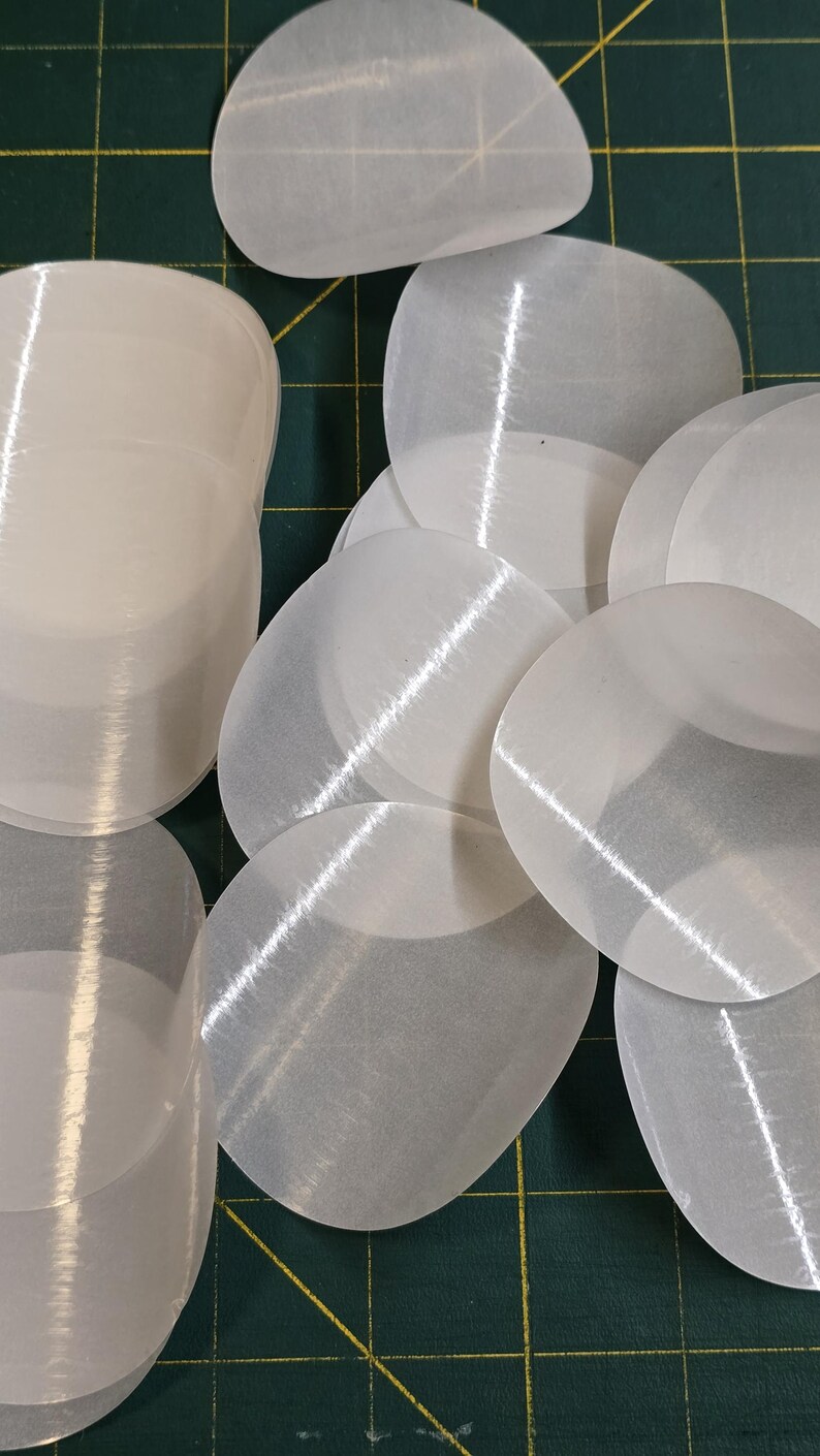 May include: A collection of translucent, oval-shaped, white objects. The objects are arranged on a green cutting mat with yellow grid lines. The objects have a slightly textured surface and appear to be made of a thin, flexible material.