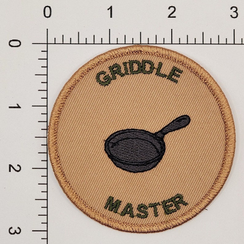 May include: A tan and green embroidered patch with the text "GRILL MASTER" and a black and white illustration of a frying pan.