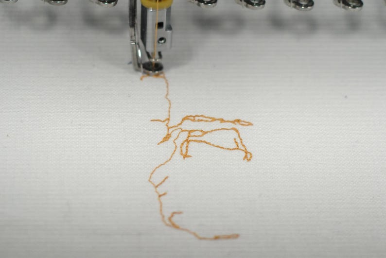 May include: Close-up of an embroidery machine in operation, stitching a design with orange thread onto white fabric. The needle is visible, creating the pattern. The image highlights the process of textile art.