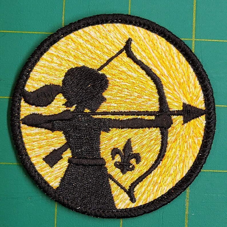 May include: A black embroidered patch with a silhouette of a person holding a bow and arrow. The background is yellow with white stripes. A fleur-de-lis is in the lower right corner.
