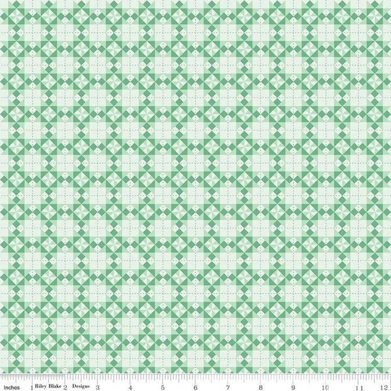 Pode incluir: Um tecido com um padr&atilde;o geom&eacute;trico repetitivo de losangos verdes e verde claro. O design &eacute; definido em um fundo claro com uma grade de linhas pontilhadas. A parte inferior da imagem tem uma r&eacute;gua com polegadas e o texto "Riley Blake Designs".