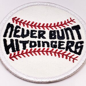 May include: White embroidered baseball patch with red stitching and the text "Never Bunt Hittingers" in black.
