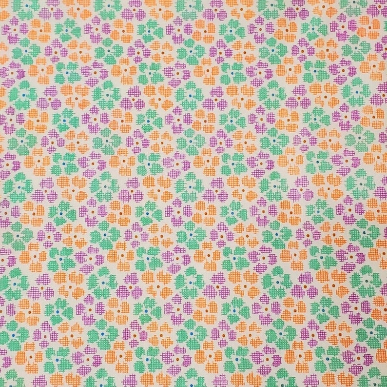 May include: A patterned fabric featuring a repeating floral design. The flowers are made up of small, cross-hatched lines in orange, green, and purple, set against a cream background. The design is evenly spaced, giving a textured look.