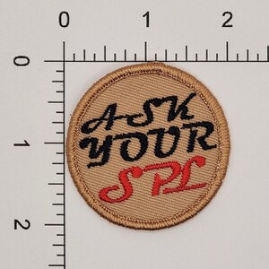 May include: A round brown patch with the text "Ask Your SPC" embroidered in black and red thread.