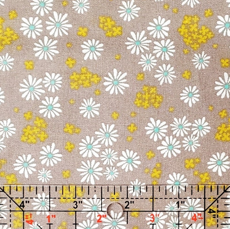 May include: A brown fabric with a white daisy pattern and yellow accents. The fabric is measured with a ruler in inches.