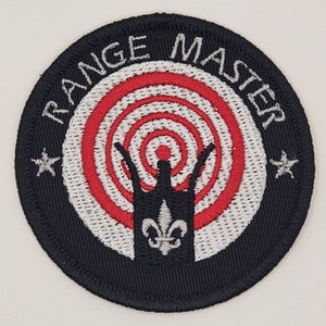 May include: Black embroidered patch with a white circle containing a red and white target with a black crown in the center. The text "RANGE MASTER" is written in white around the circle.
