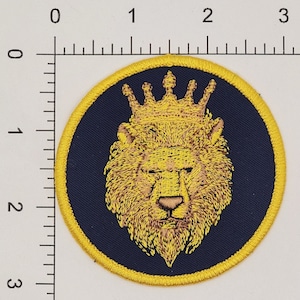 Puede incluir: Una cabeza de le&oacute;n bordada en amarillo con una corona dorada sobre un fondo azul oscuro. La cabeza de le&oacute;n est&aacute; rodeada por un borde amarillo.