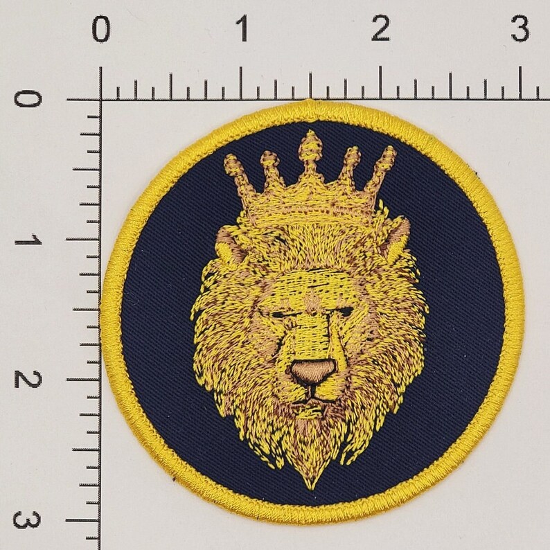 Puede incluir: Una cabeza de le&oacute;n bordada en amarillo con una corona dorada sobre un fondo azul oscuro. La cabeza de le&oacute;n est&aacute; rodeada por un borde amarillo.