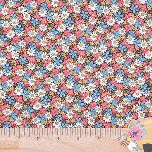 May include: A brown fabric with a repeating pattern of small white, blue, and pink flowers. A wooden ruler with inch markings is placed at the bottom of the image.