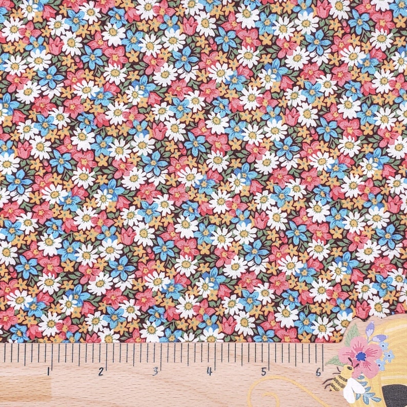 May include: A brown fabric with a repeating pattern of small white, blue, and pink flowers. A wooden ruler with inch markings is placed at the bottom of the image.