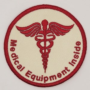 May include: Red round patch with white fabric in the center. The patch has a red medical symbol with wings and the text "Medical Equipment Inside".