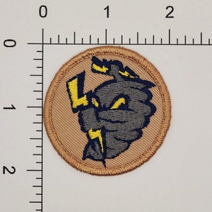 May include: Round embroidered patch featuring a gray and navy blue cartoon character with yellow lightning bolts. The patch is approximately 2 inches in diameter and has a tan border.